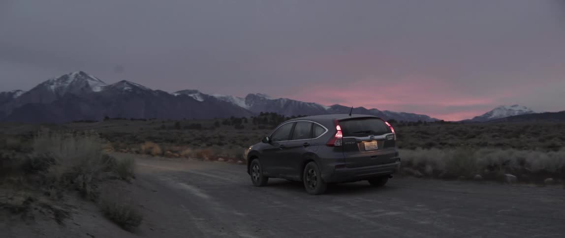 Dark SUV driving on a dirt road during a cinematic sunset with mountain background.