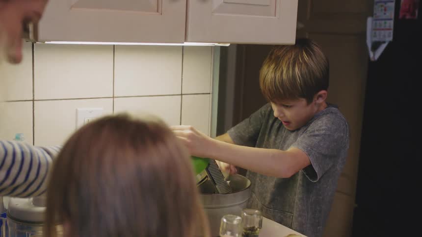 A woman helps her son use a box grater as they cook at home