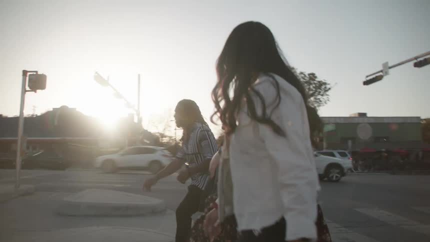 Friends walk across intersection as sun glares from sky