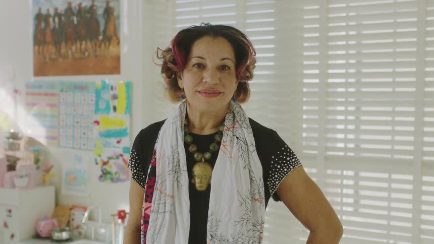 A woman posing with a soft smile on her face in a bright room with childrens artwork behind her