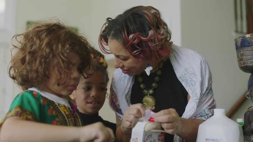A woman opens a package as she cooks with her children at home