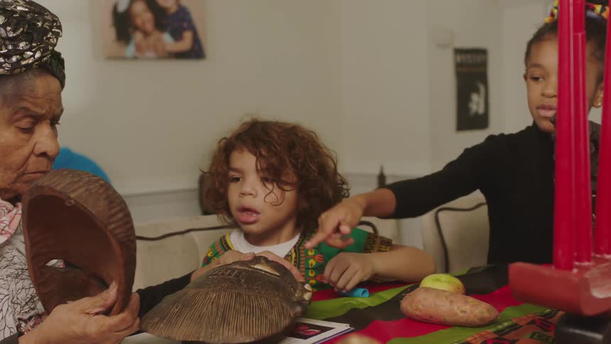 An elderly woman shows small children heritage masks