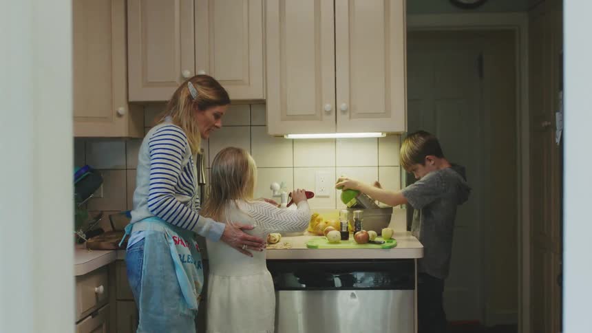 A woman rubs her daughters back while helping her use a peeler at home