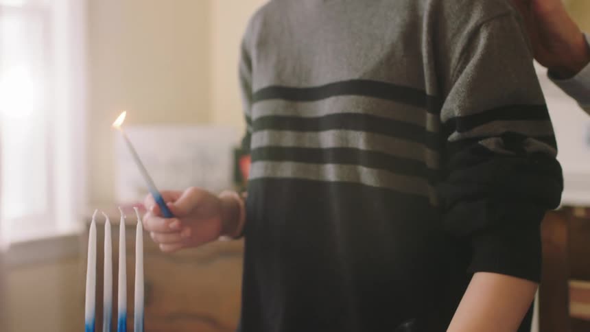 A woman uses a candle to light other candles on a cake