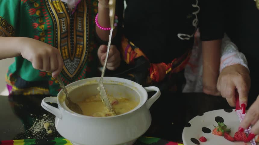 A woman helps her daughters create a dish with strawberries and cream