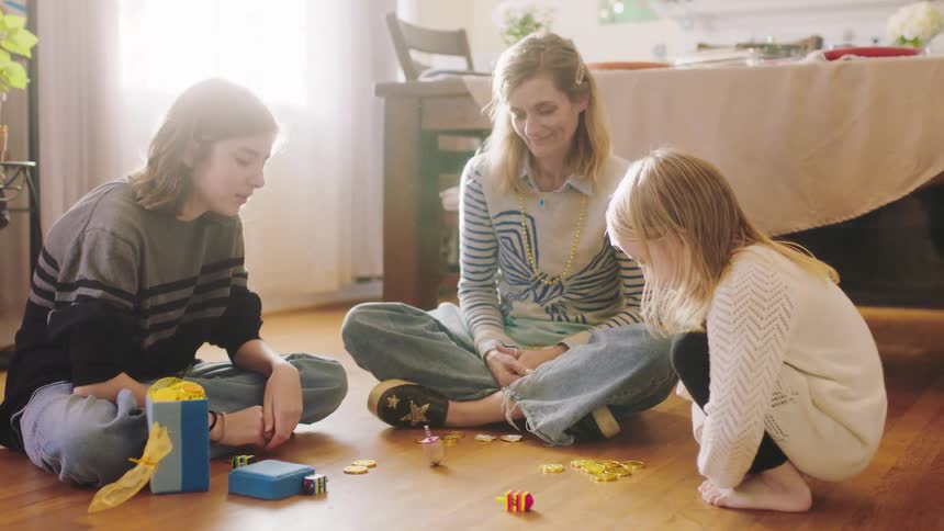 A mother sits on the floor at home with her children and they play a game