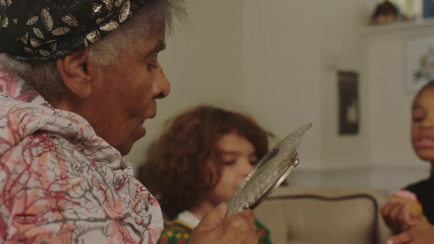 An elderly woman reads a book to a young boy and girl as they eat a cupcake