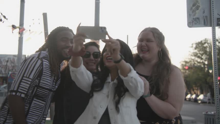 A woman holding up a phone taking a selfie with a group of smiling laughing friends