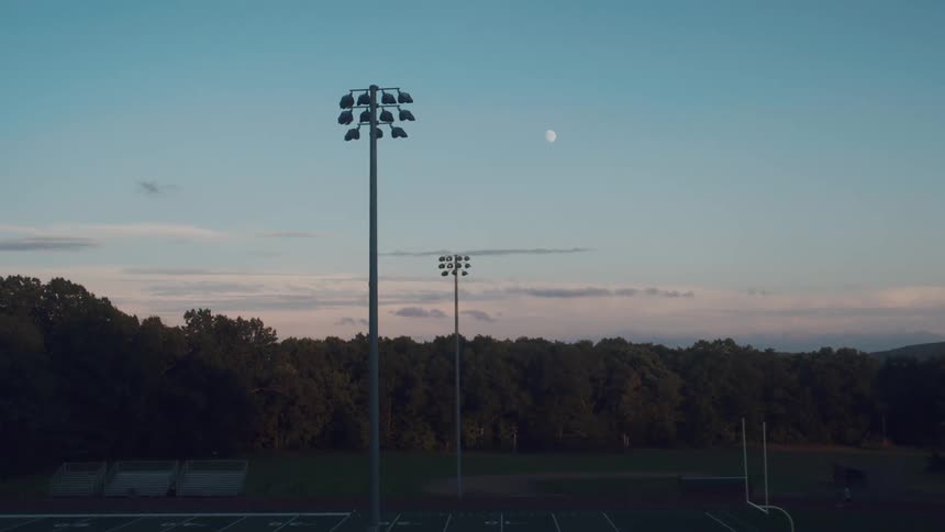 Moon sits over woods and nearby football field