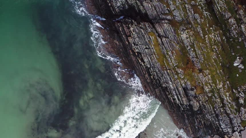 Ocean waves are crashing against rock layers on the coast