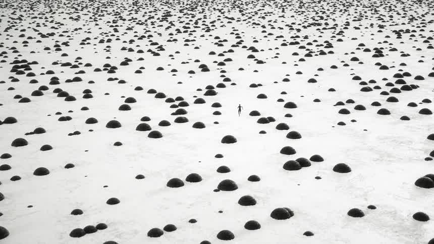 A humanoid figure runs quickly past black mounds on a white surface