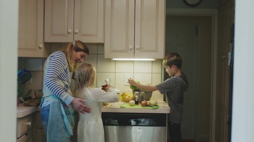 Mother teaching her son how to grate a raw potato on the kitchen at home