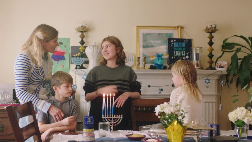 Mom smiles encouragingly as her oldest child talks after lighting the menorah