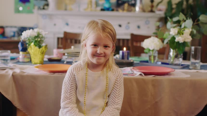 A young girl sits at a table with party decorations behind her