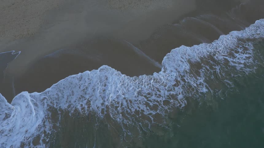 Aerial view of waves rolling over a beach splashing and foaming