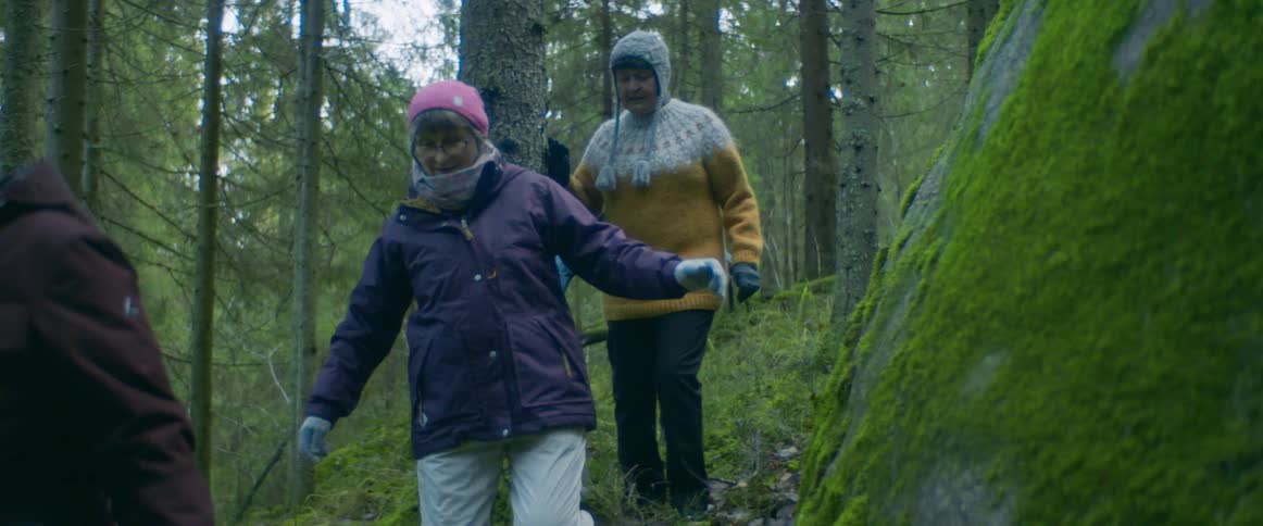 A group of elderly women hike through a forest during the day