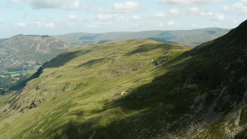 A paraglider floats serenely above green slopes