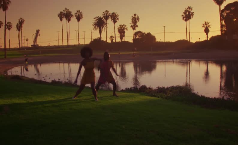 A man and woman dance on the grass near a pond at sunset