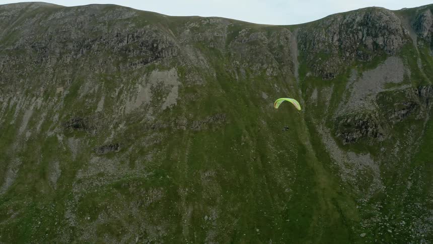 A person paraglides past a large hill