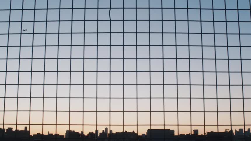 Airplane flying over the skyline of a city behind a wired fence at sunset