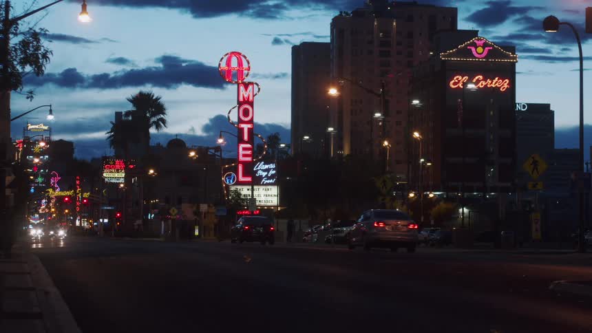 Traffic passes down a city street lit up with neon signs