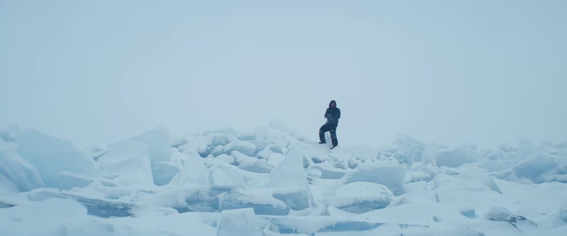 A person wearing a black snow suit is climbing on chunks of ice in the arctic