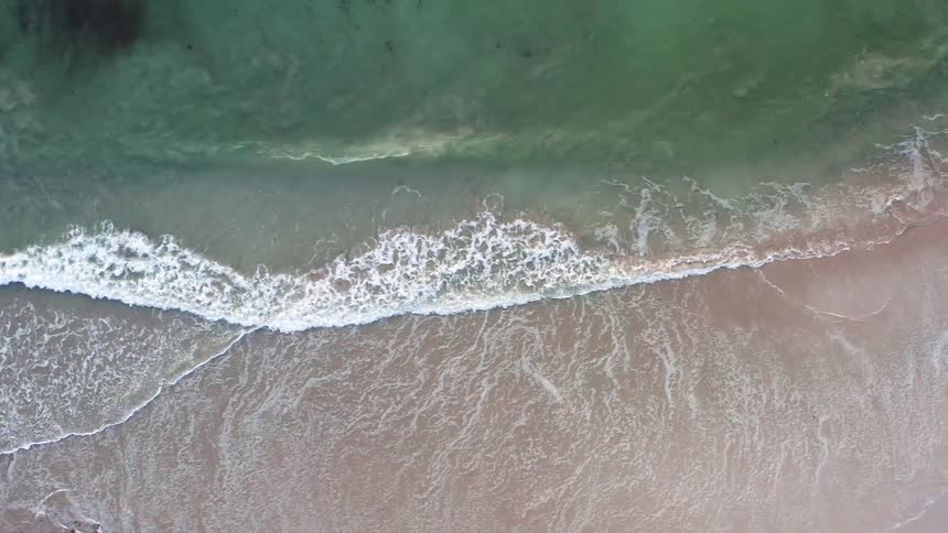 Ocean waves washing ashore a brown sandy beach