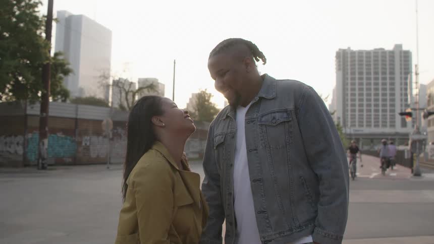 A woman holds a mans hand and looks up at him and hugs him as they stand in front of people on bicycles on a city street