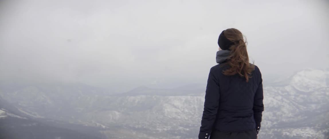 A woman is standing viewing a large mountain range below
