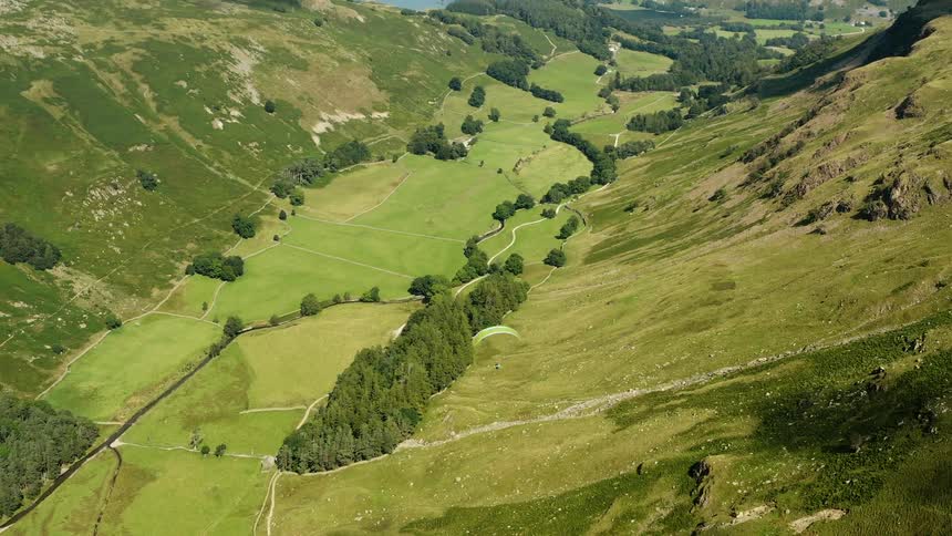 Aerial view of a person paragliding over a valley between the mountains close to a lake
