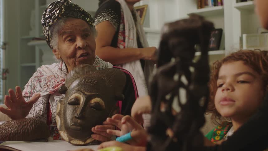 Siblings listen as grandmother talks about mask and mother walks by