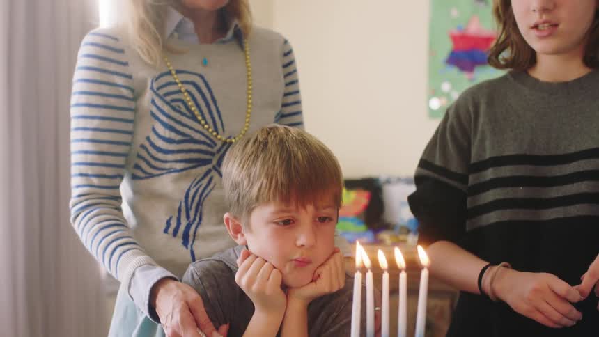 Blonde grandmother with white and blue sweater holds grandson waiting to candle on birthday cake