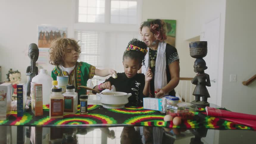 A woman helps her daughters cook and mix ingredients at home