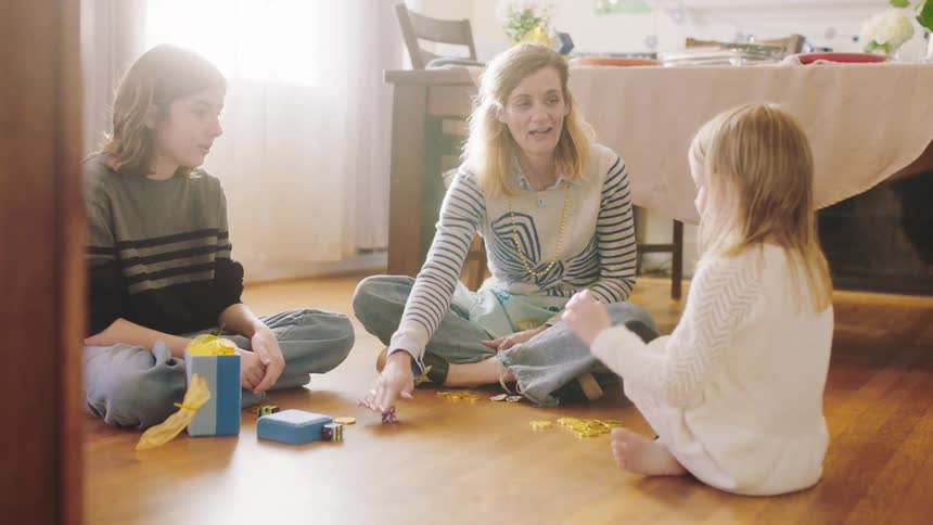 Mother and daughters sit on floor near dining table playing a game