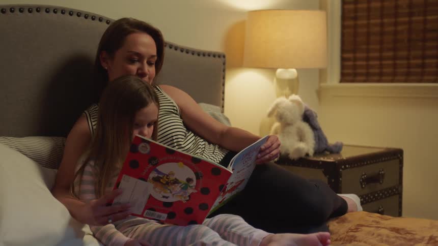A woman sits in bed with her daughter and reads to her