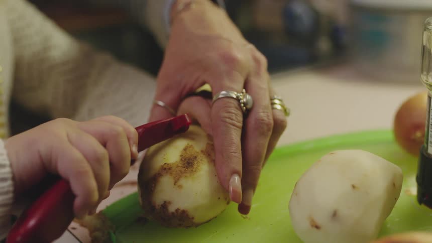 A woman helps her daughter peel a potato at home