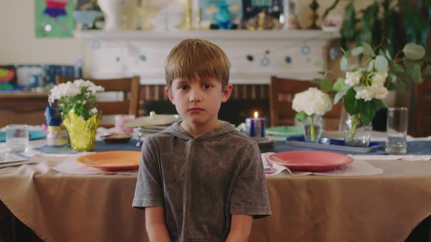 Young boy sitting in front of the table at home looks at the camera