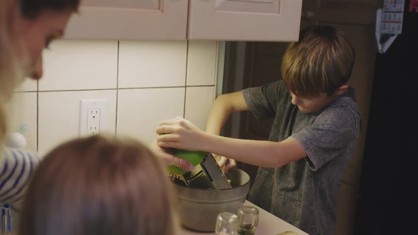 Mother teaching her son how to grate a raw potato on the kitchen at home