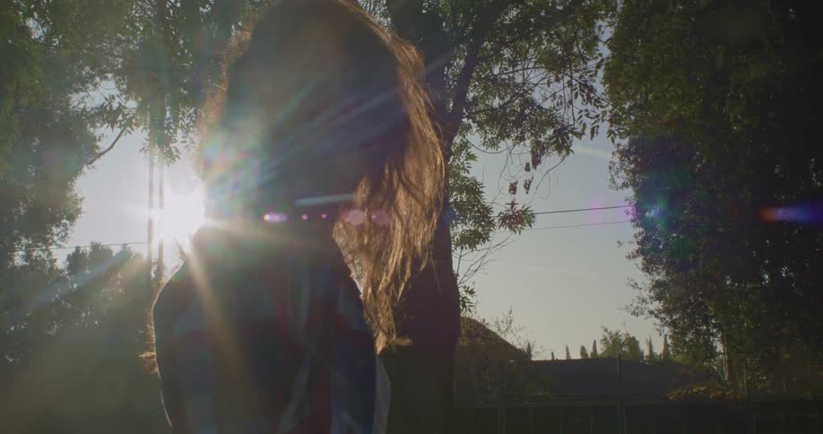 Young woman standing on the park turns around to look at the camera at sunset