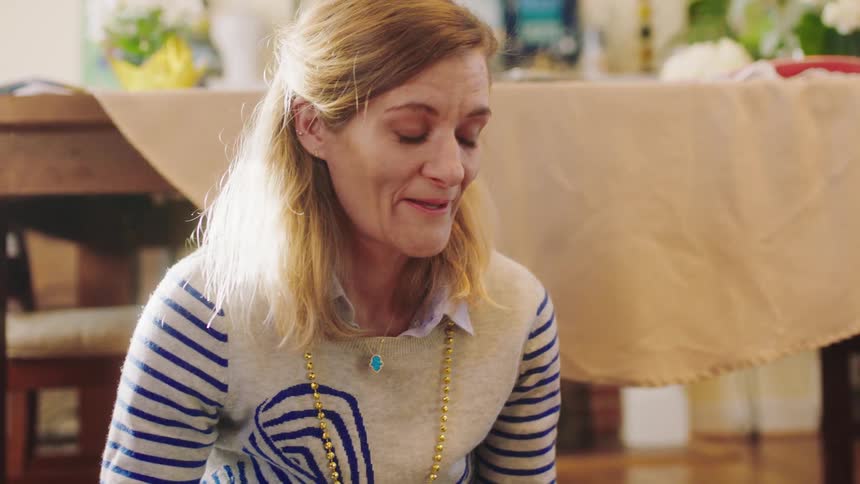 Mother sits on floor near dining table talking and smiling with family