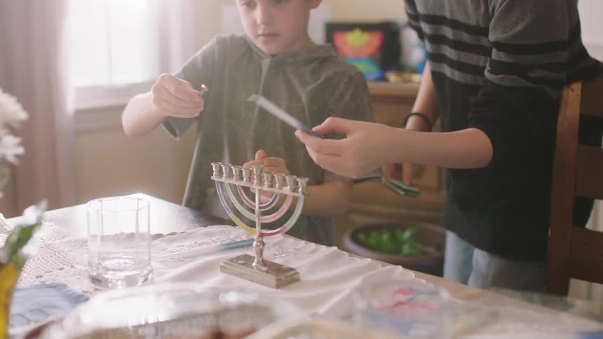 Sister helps younger brother to burn the back of a candle to be placed on a menorah