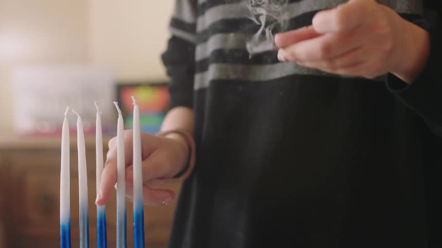 A woman holds a lit match in front of candles and then raises the match to it out