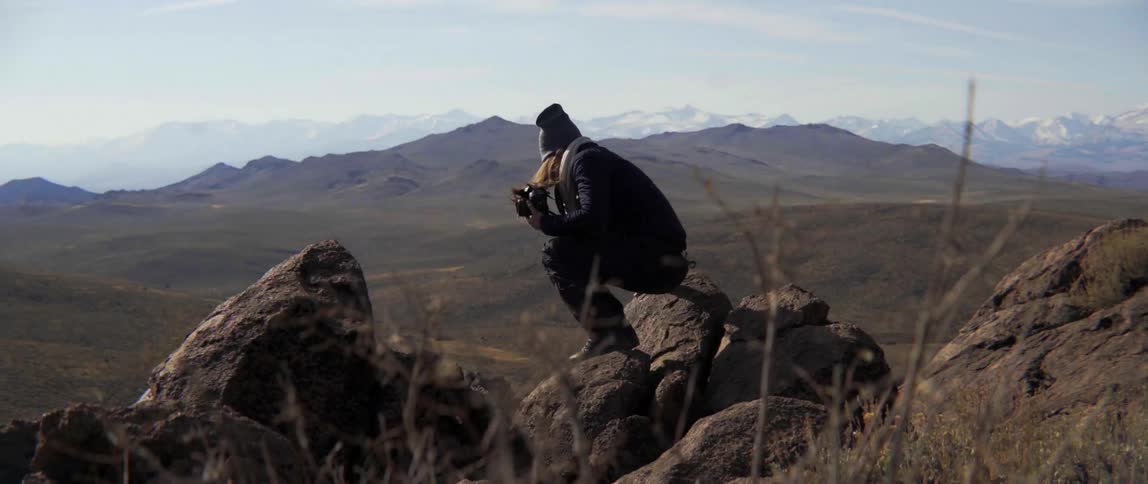 A woman sits on some rocks on a windy mountain top