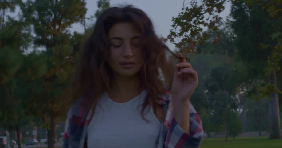 Young woman on a park at sunset walking backwards looking at the camera