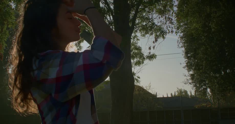 Woman with flannel shirt touches brown wavy hair in the public park