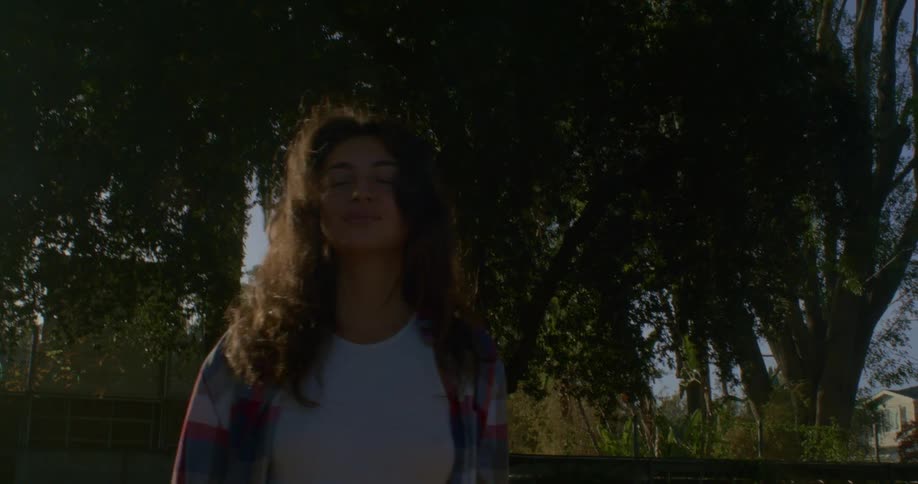 Woman with brown wavy hair and flannel shirt wanders in public park