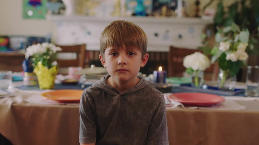 Young boy sitting in front of the table at home looks at the camera