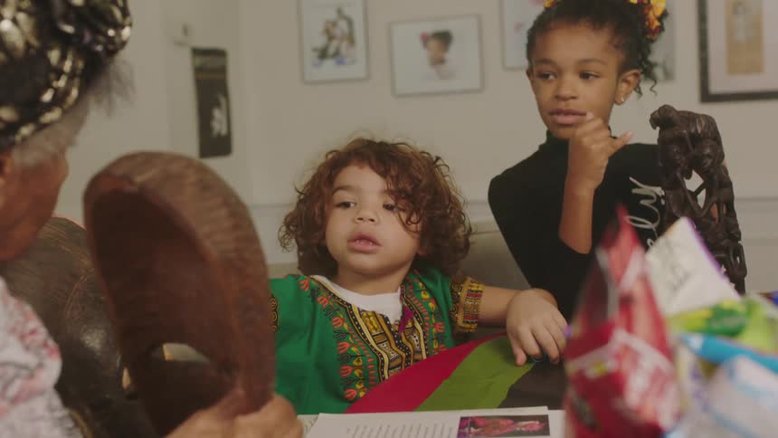 Grandmother talks to kids about carved wooden face masks as they sit at table