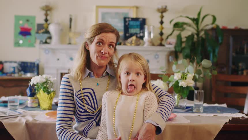 A young girl makes a silly face while sitting on her mothers lap