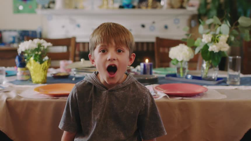 Young surprised boy sitting in front of the table at home looks at the camera with his mouth open